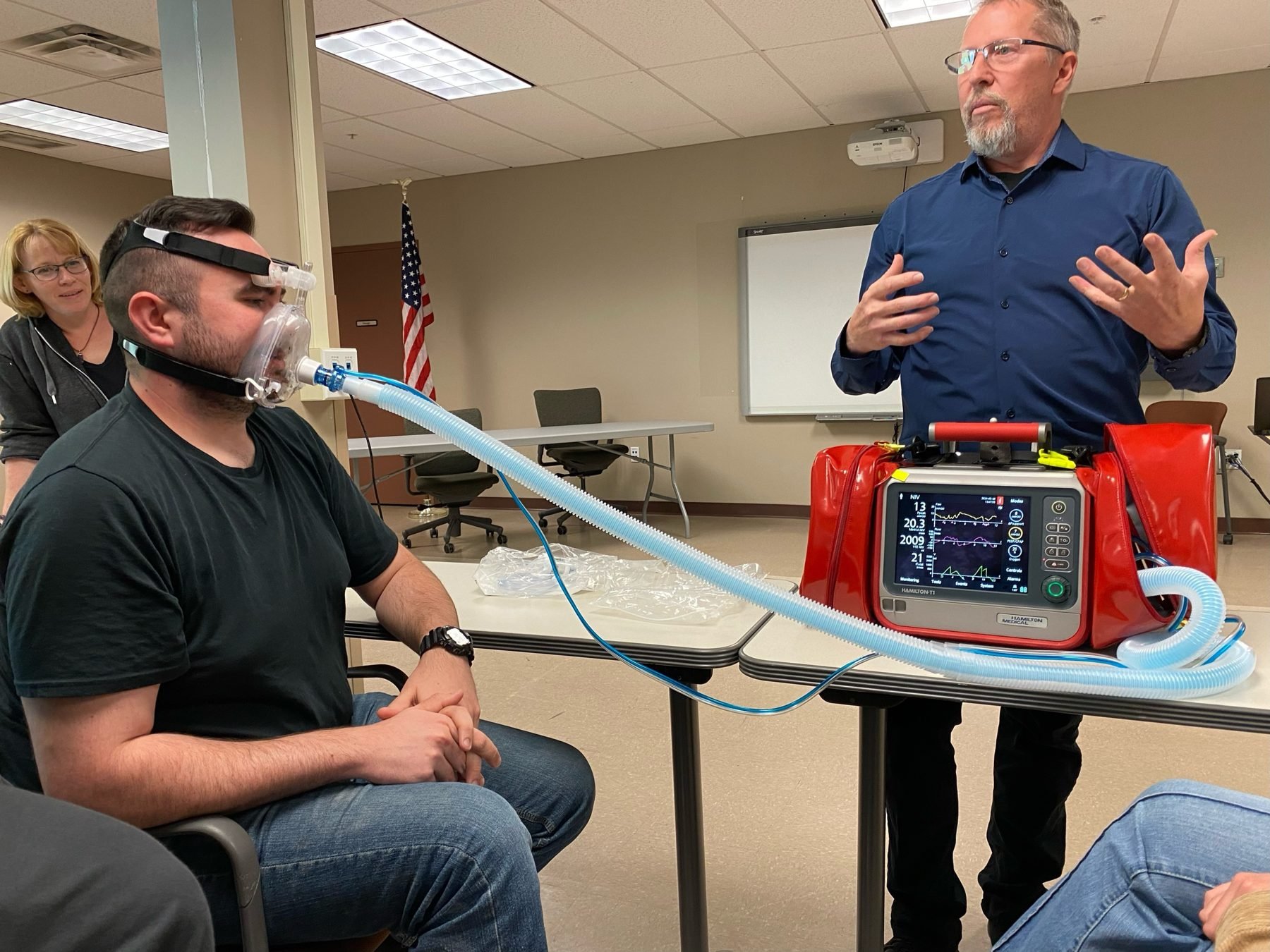 Paramedic William O'Connor wearing a BiPAP full-face mask during a training demonstration while ALS Coordinator Mark Foster explains the settings
