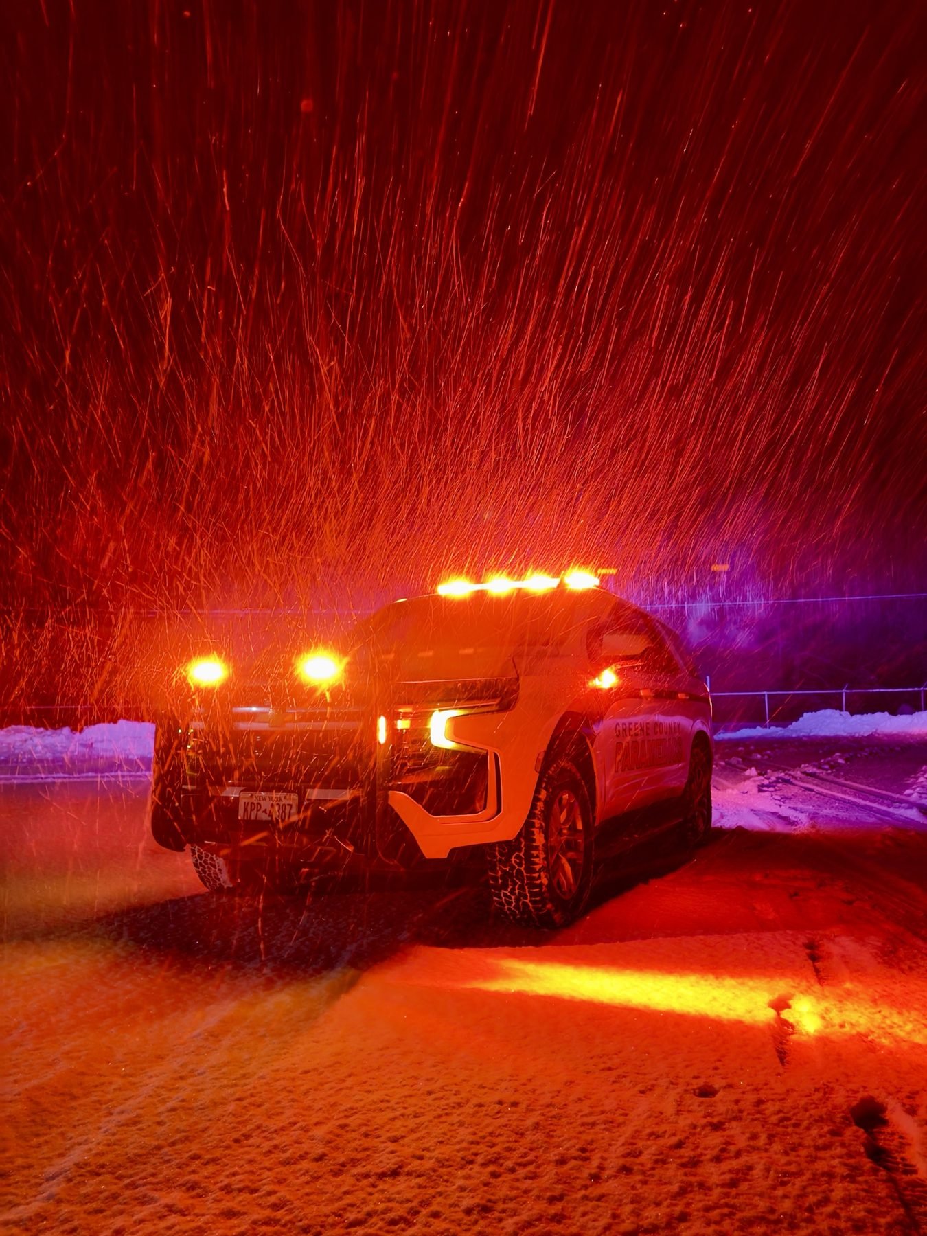 A GCEMS fly car in a night snowstorm, emergency lights glowing through the snow